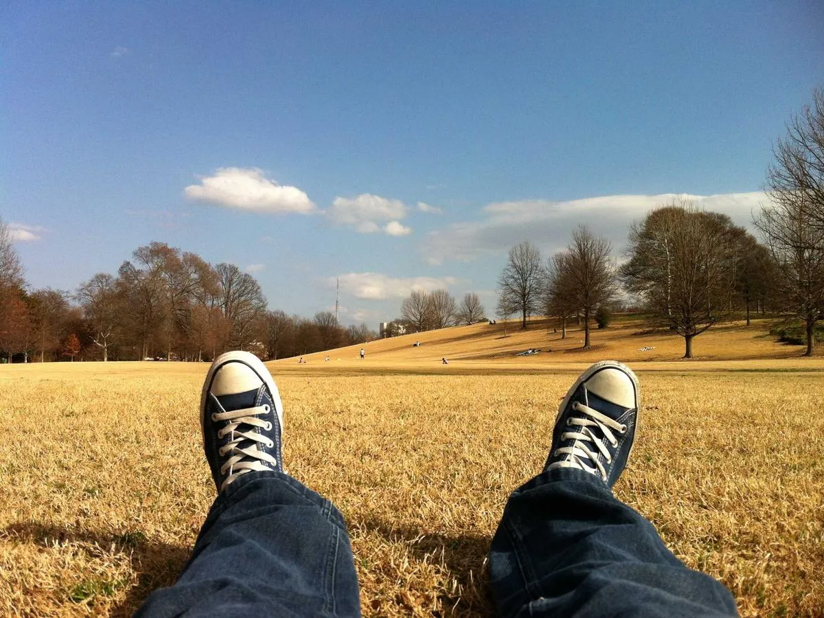 Two feet in canvas sneakers, resting on dry grass under a blue sky.